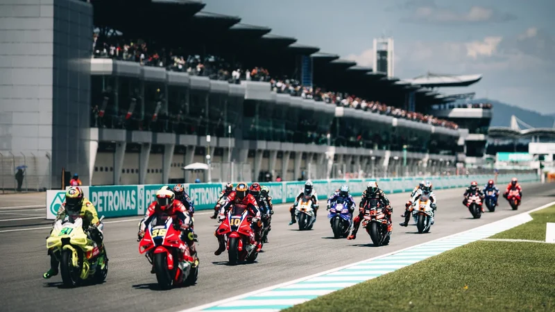 Para pembalap MotoGP melaju di lintasan Petronas Sepang International Circuit dengan Main Grandstand yang penuh penonton di sisi kiri