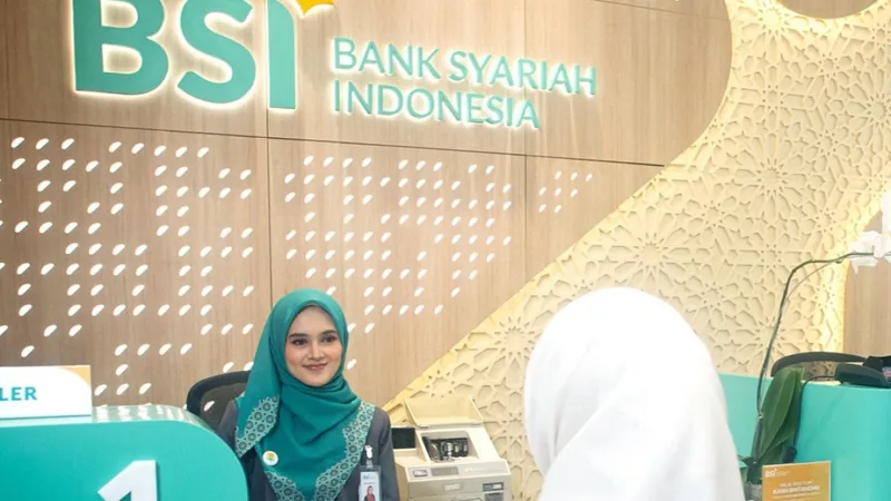 Petugas BSI melayani nasabah di kantor cabang Bank Syariah Indonesia dengan logo BSI di dinding