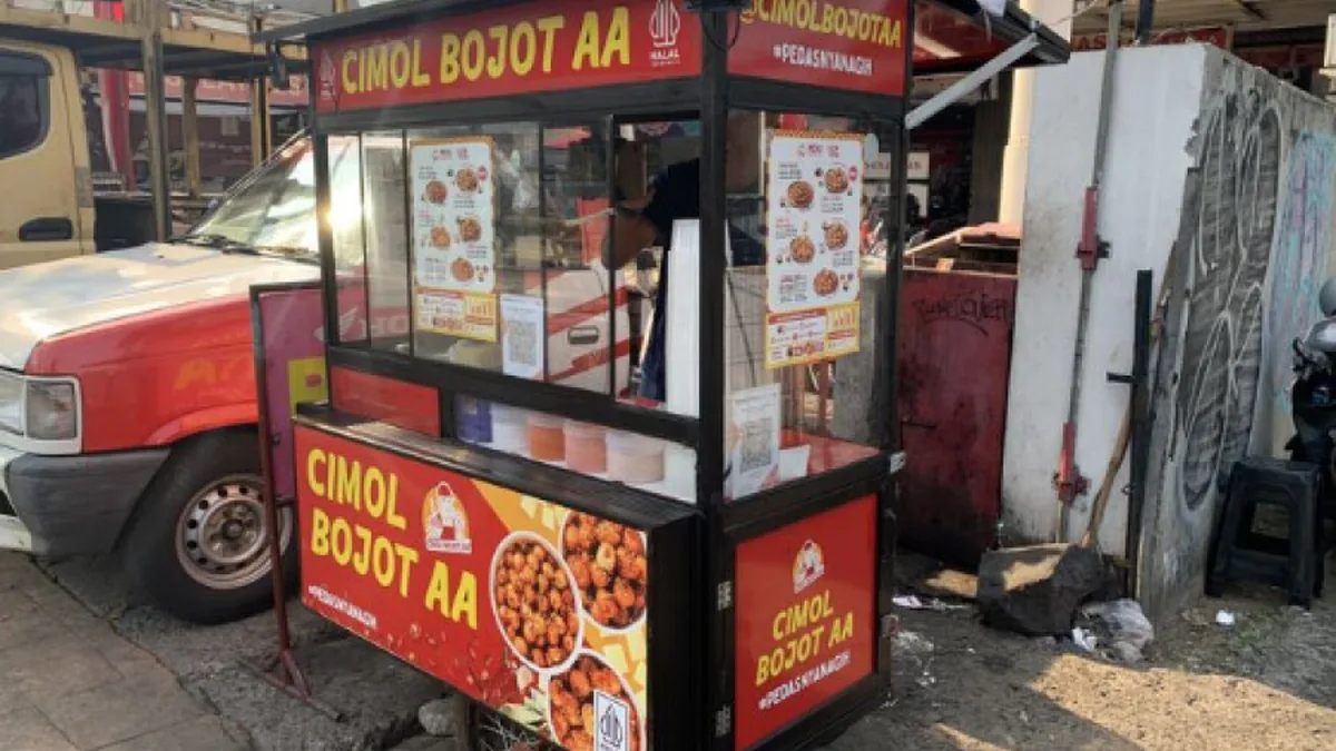 Gerobak resmi Cimol Bojot AA dengan papan nama merek berwarna kuning di atas latar merah, logo halal, dan kode QRIS pada kaca etalase