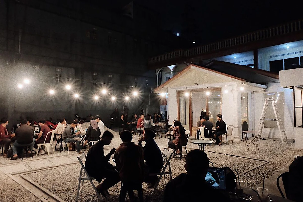 Suasana kedai kopi outdoor Jakarta pada malam hari dengan lampu gantung dan pengunjung