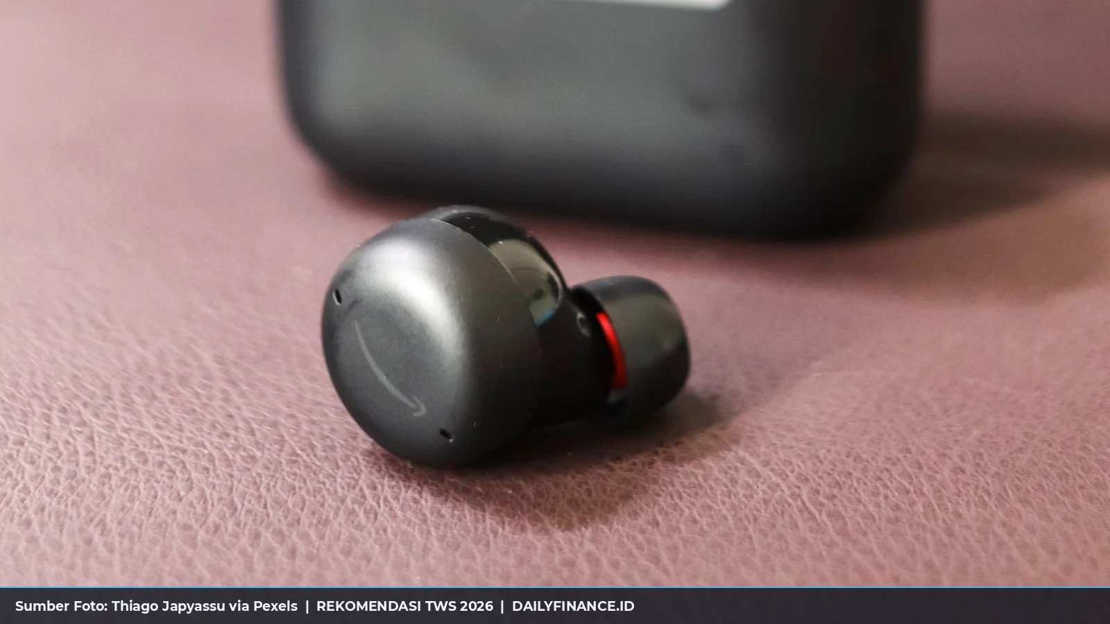 Earphone nirkabel true wireless stereo hitam dengan charging case di atas permukaan kain
