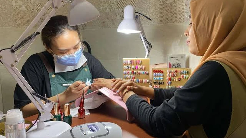 Teknisi seni kuku sedang melukis kuku pelanggan dengan kuas detail di studio salon kuku