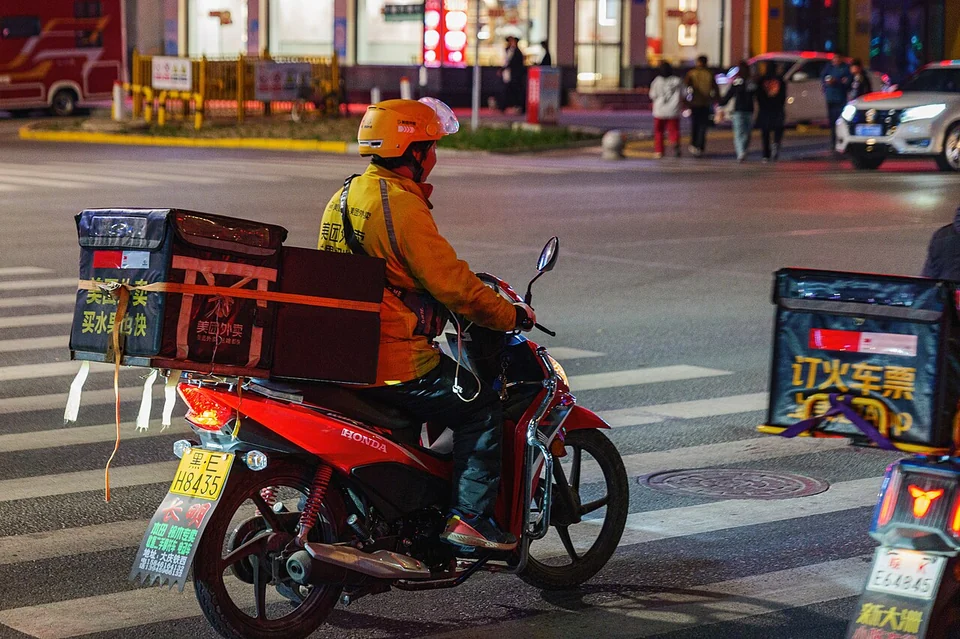 Kurir pengantaran makanan melintas di jalan dengan kotak pesanan