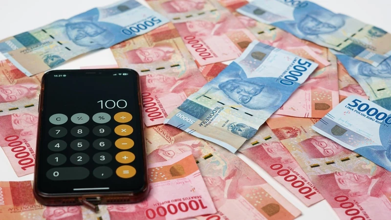 Uang pecahan rupiah seratus ribu dan lima puluh ribu dengan ponsel pintar menampilkan layar kalkulator