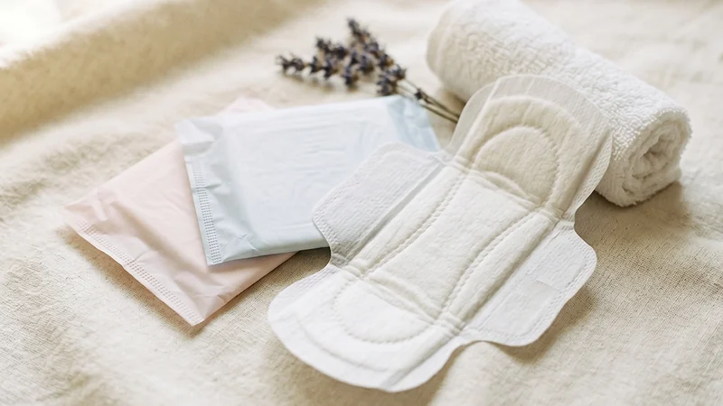 Produk sanitasi menstruasi berupa pembalut sekali pakai dan pembalut bersegel disusun di atas permukaan kain berwarna krem