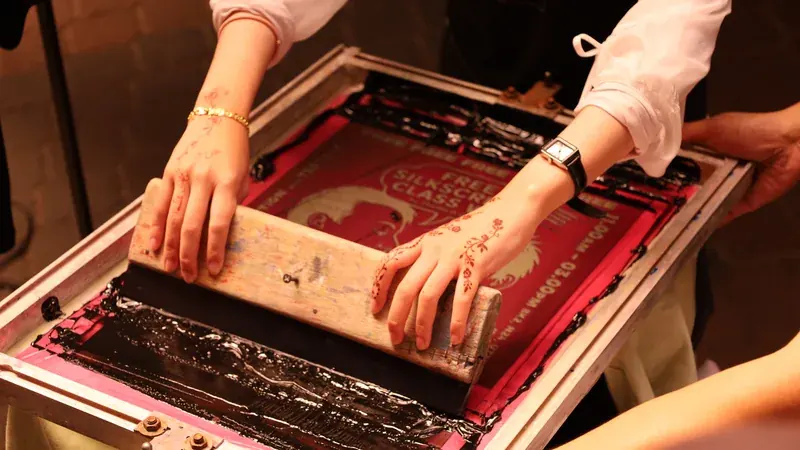 Penerapan teknik sablon manual menggunakan rakel dan pasta tinta pada bidang kain kaos