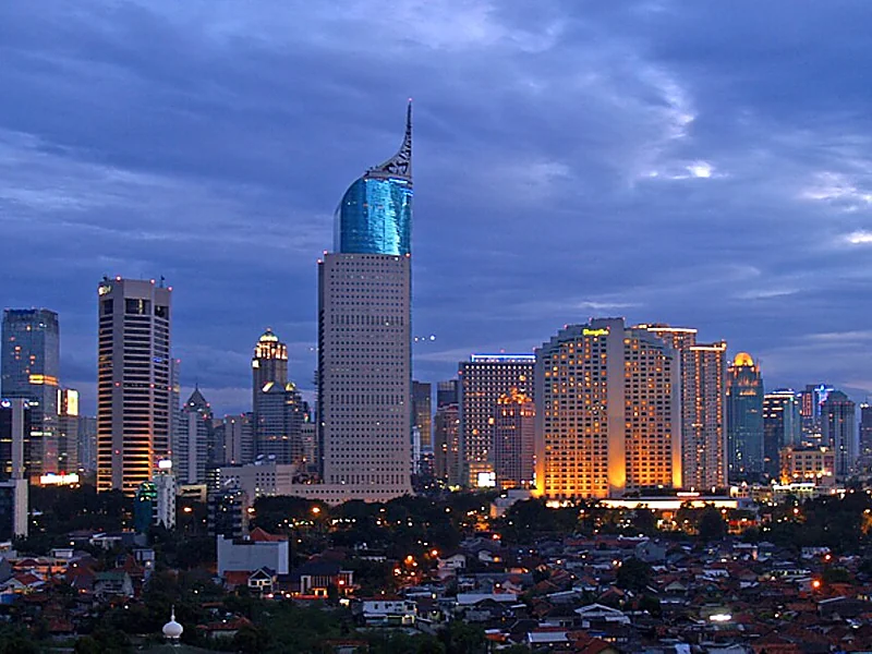 Pemandangan senja Jakarta dengan Wisma 46 atau Kota BNI dan Hotel Shangri-La Jakarta di kanan, di depan permukiman padat