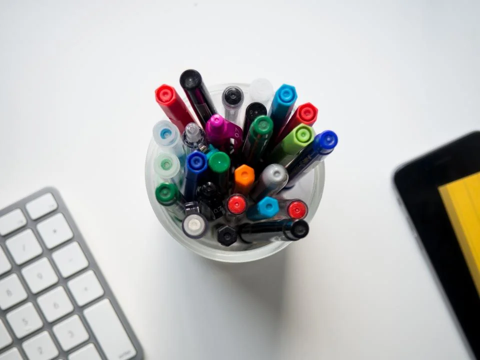 Cangkir berisi spidol dan pulpen warna-warni di meja kerja untuk color coding budget