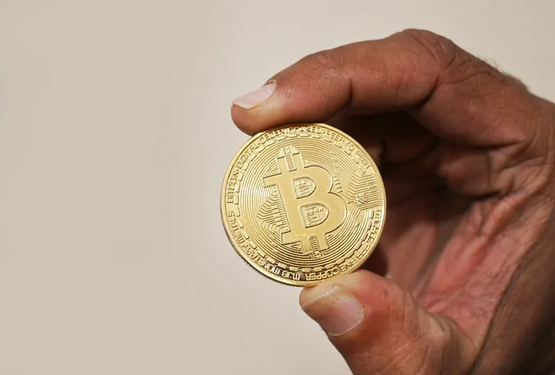 Tangan memegang koin fisik emas Bitcoin sebagai simbol disiplin menabung dan kepemilikan aset kripto jangka panjang