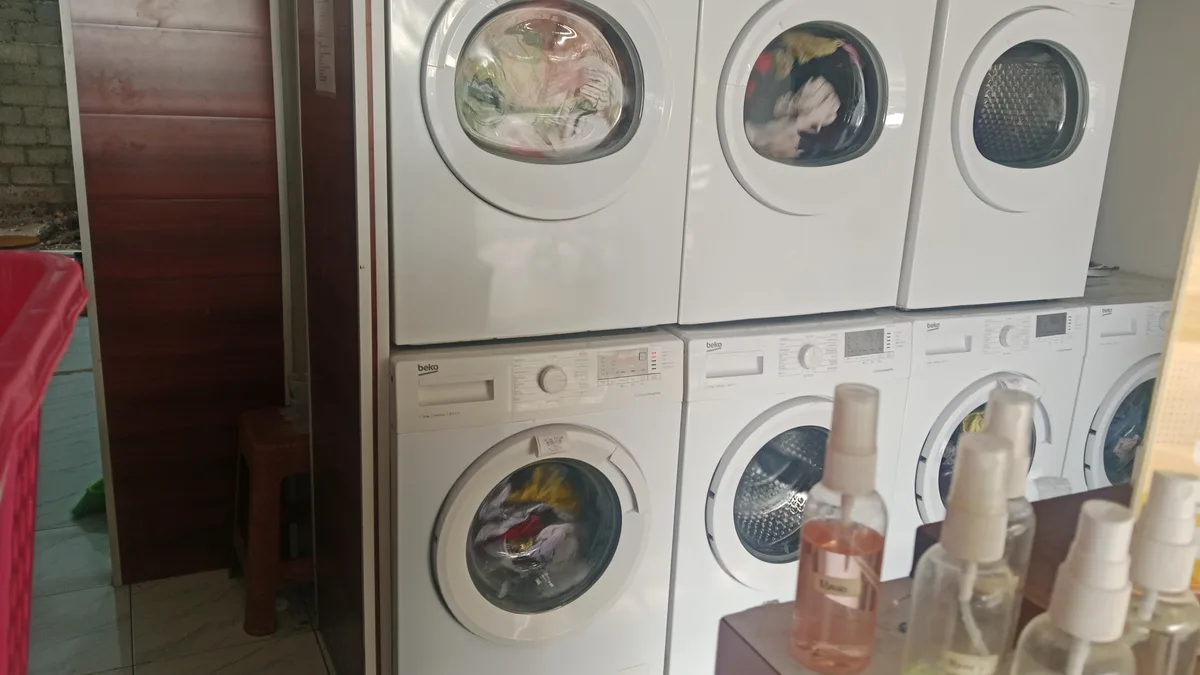 Jajaran mesin cuci dan pengering komersial di gerai usaha laundry yang memerlukan manajemen kapasitas dan utilitas yang efisien